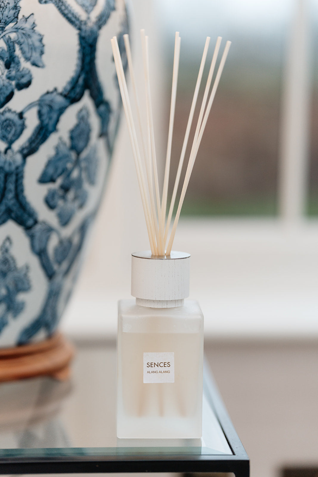 Diffuser bottle labeled 'Sences' on a table with a blurred decorative vase in the background