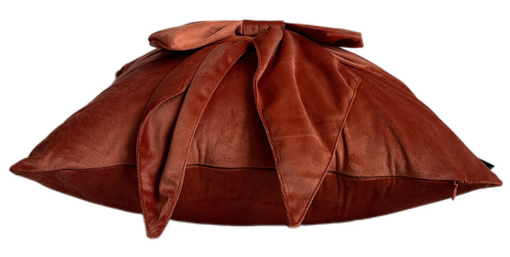 A brown velvet throw pillow with a large bow on top, shown against a plain white background.