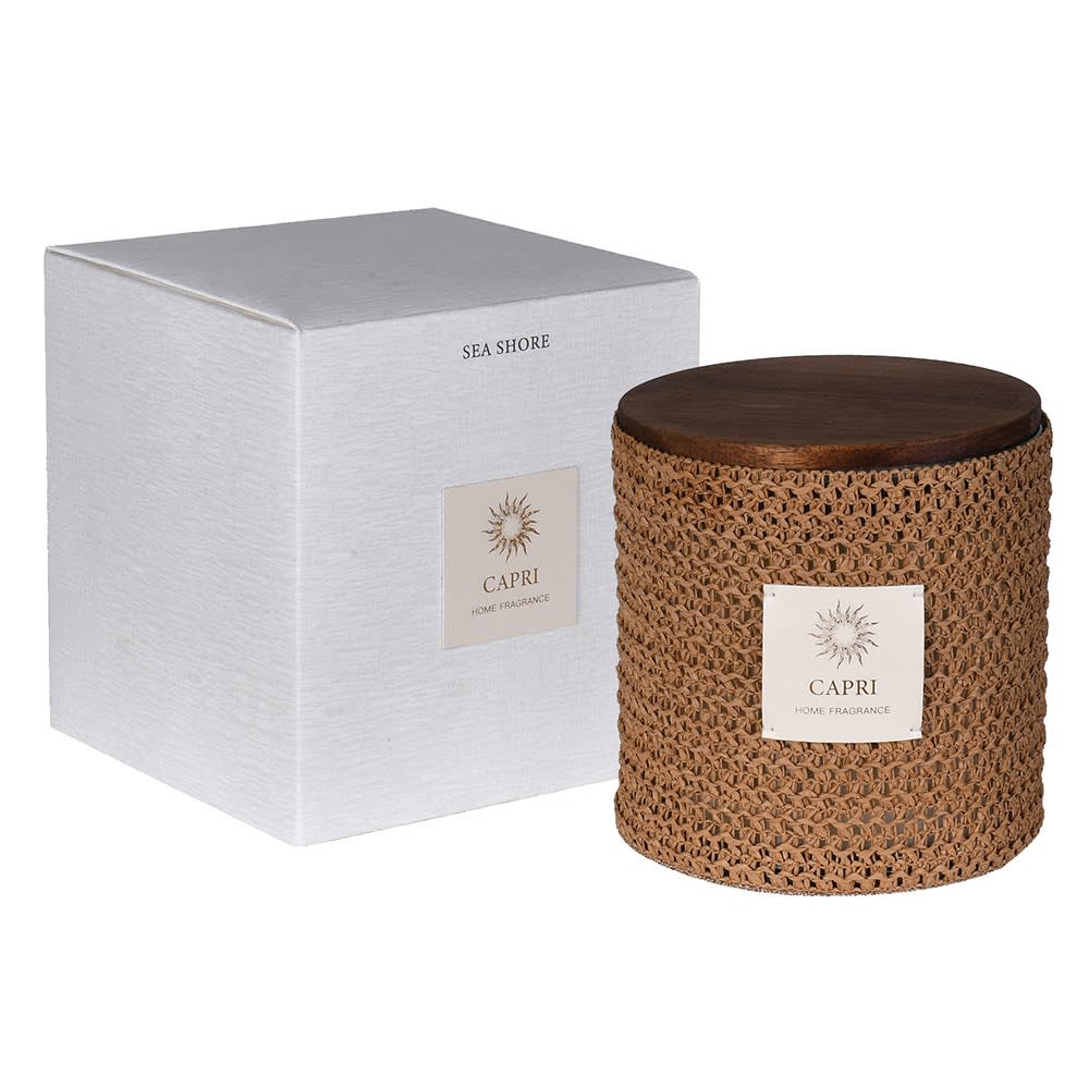 A Capri Sea Shore home fragrance candle in a woven brown jar with a dark wooden lid, shown next to its textured white packaging box.