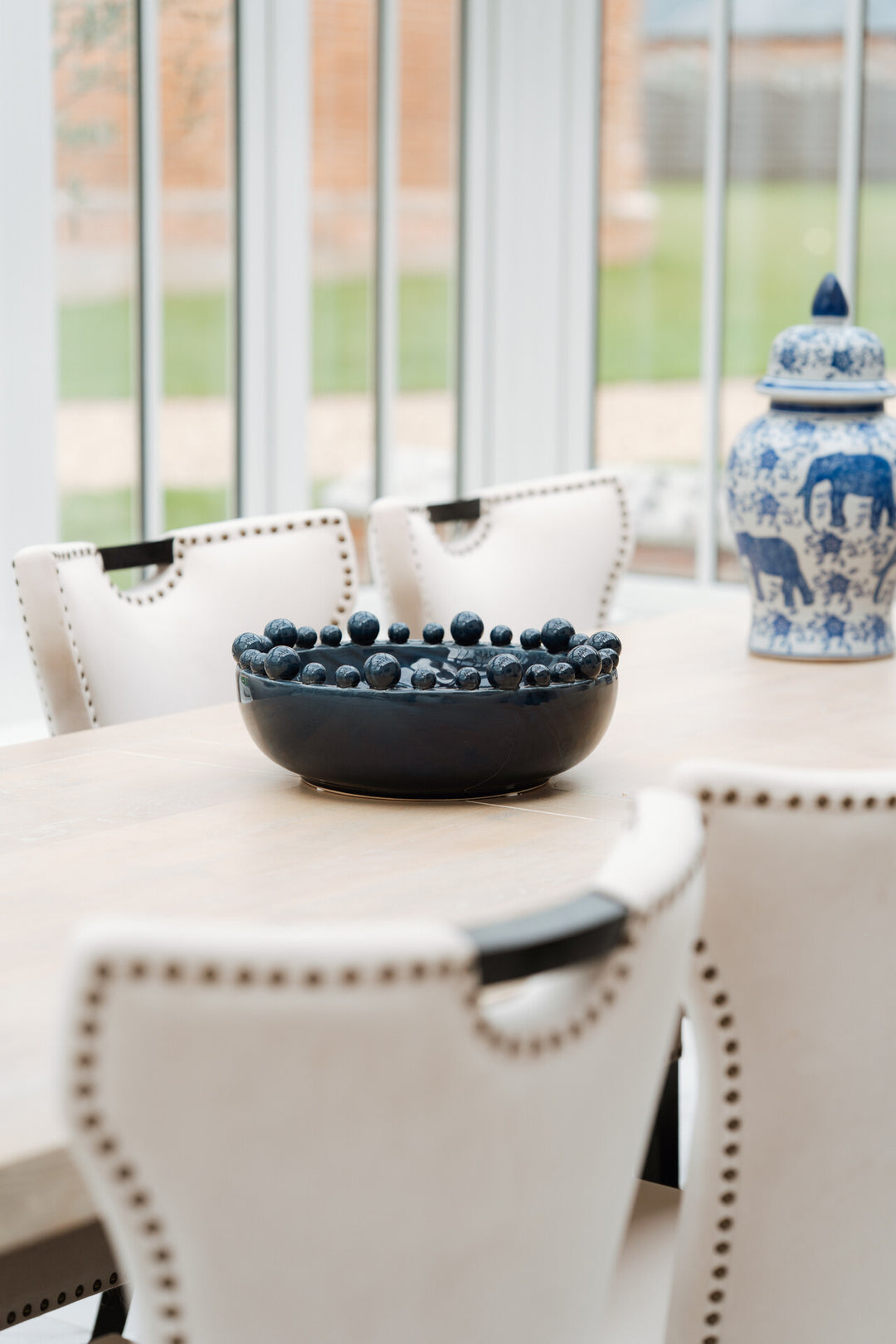 Dining table with a bowl of blueberries and a decorative jar in a bright room.