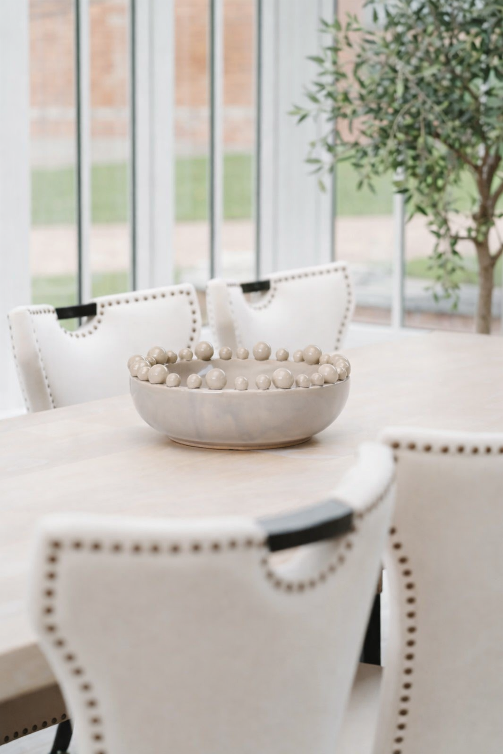 Decorative bowl with beads on a table in a room with large windows and a plant.