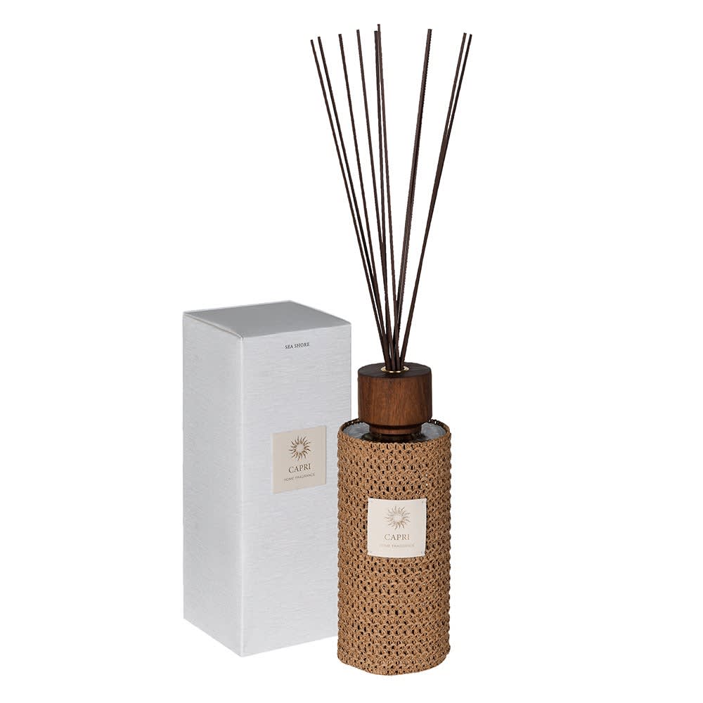 A reed diffuser bottle with a woven tan wrap, dark wood cap, and dark reeds, shown next to its white box on a white background.