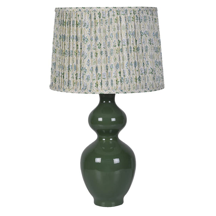 A table lamp with a glossy dark green ceramic gourd-shaped base and a pleated drum shade featuring a blue and green floral pattern on a cream background, set against a plain white background.