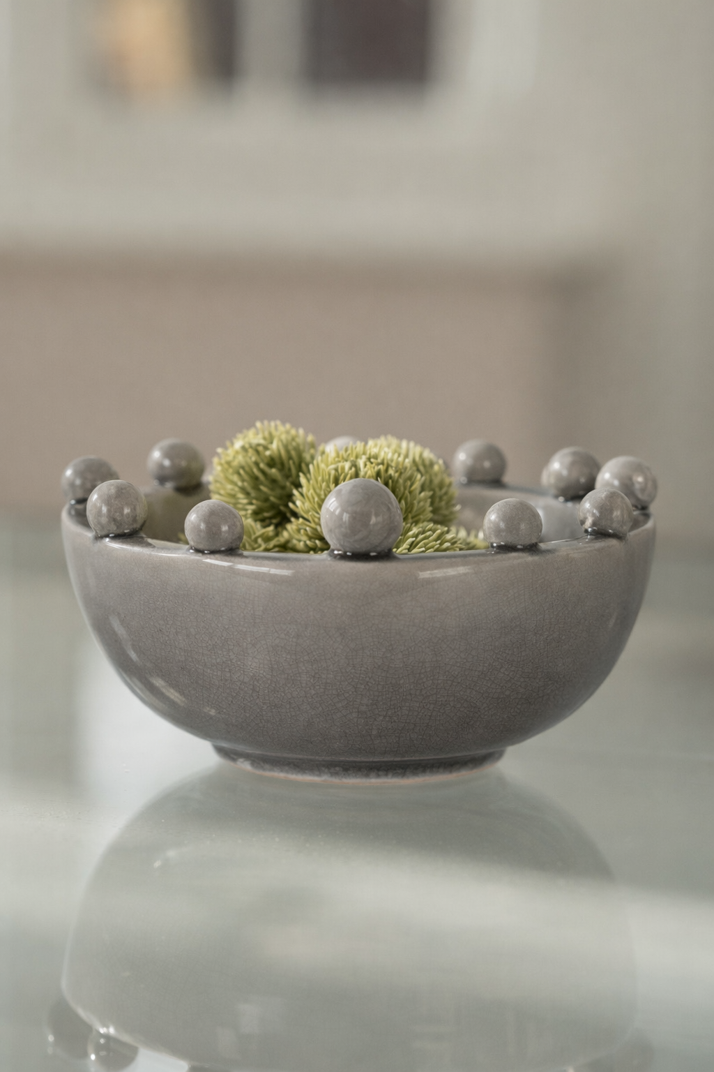 Gray bowl with decorative green and gray spheres on a reflective surface