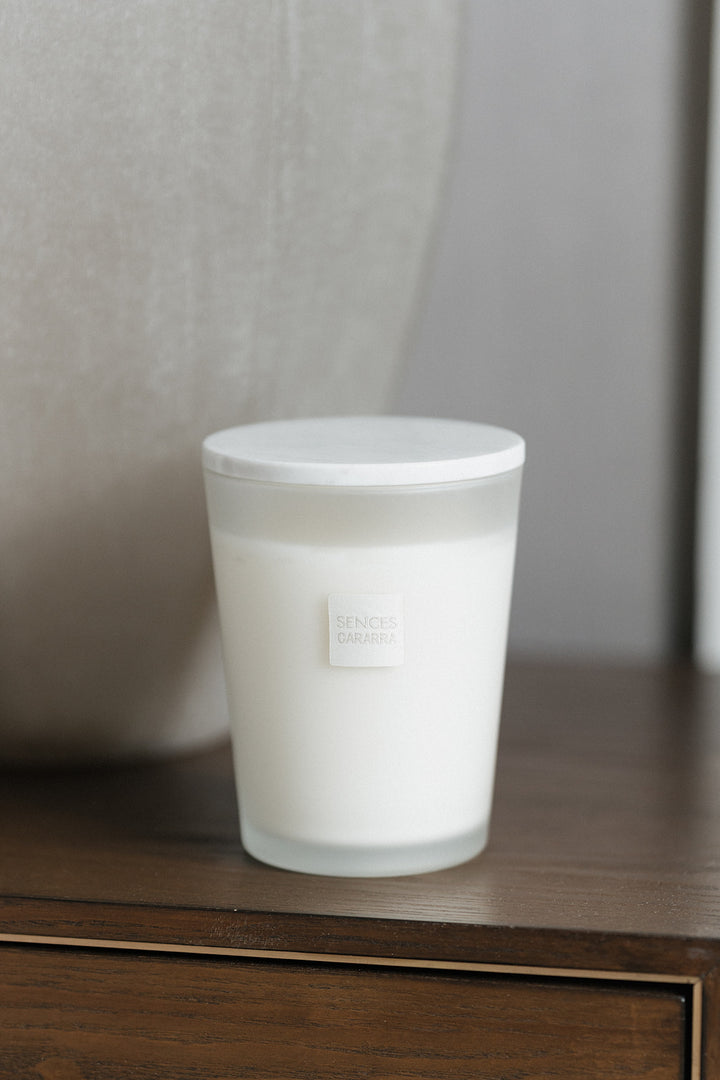 A frosted glass jar candle with a white lid and a small square label reading &