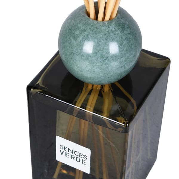 A reed diffuser with a round green stone top, natural reeds, and a square dark glass bottle. A white label on the bottle reads &