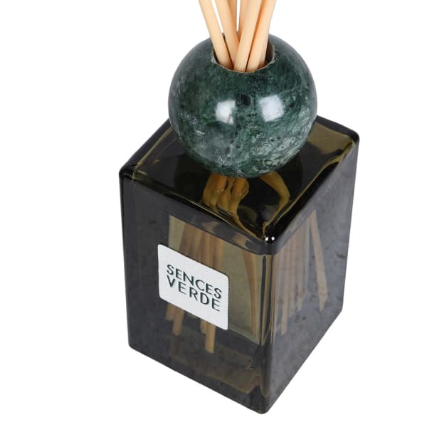 A Sentes Verde reed diffuser with a dark green marble sphere and natural wood reeds inside a translucent dark amber glass bottle with a white label.