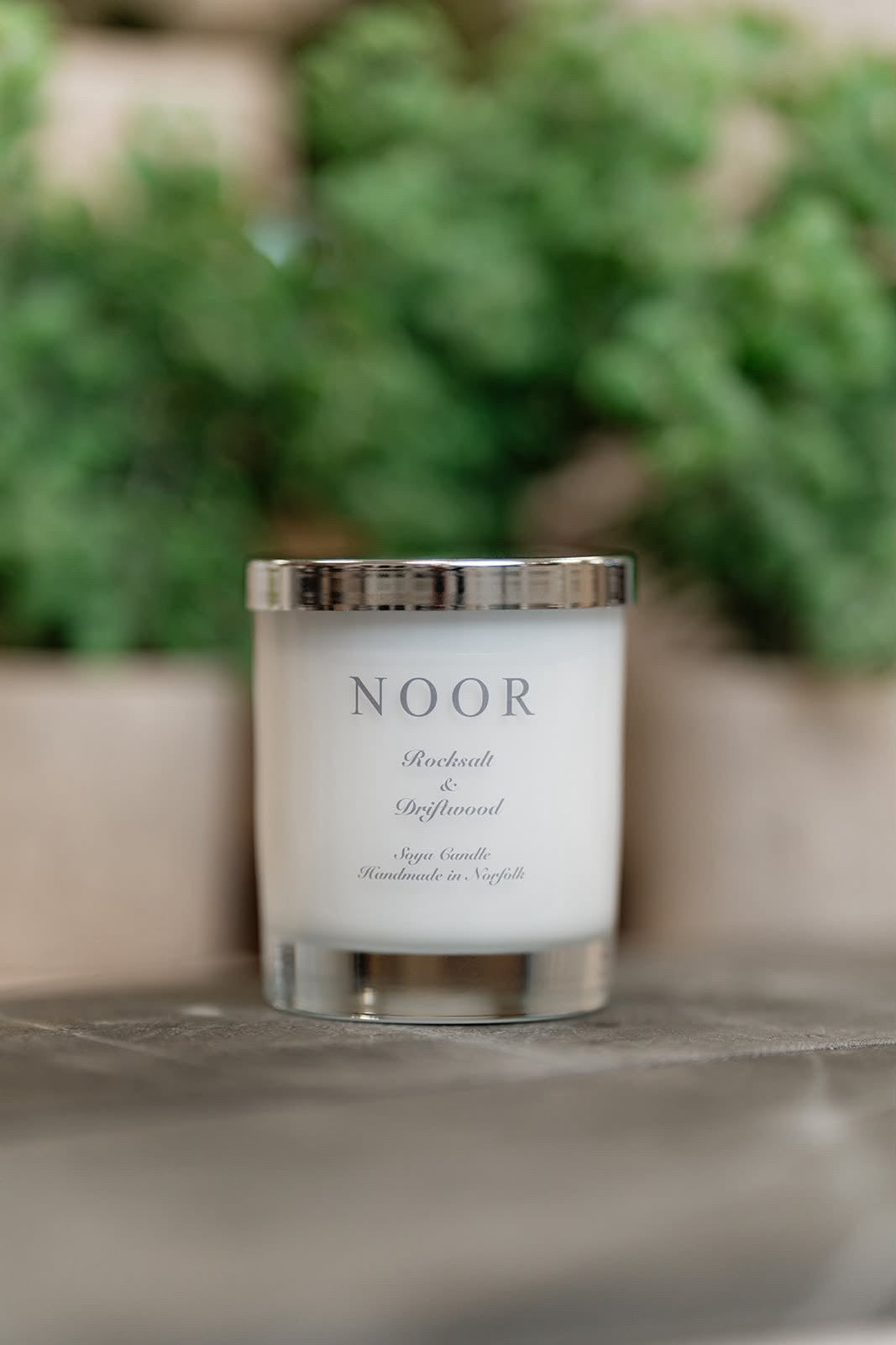 A white candle in a clear glass jar with a silver lid, labeled &