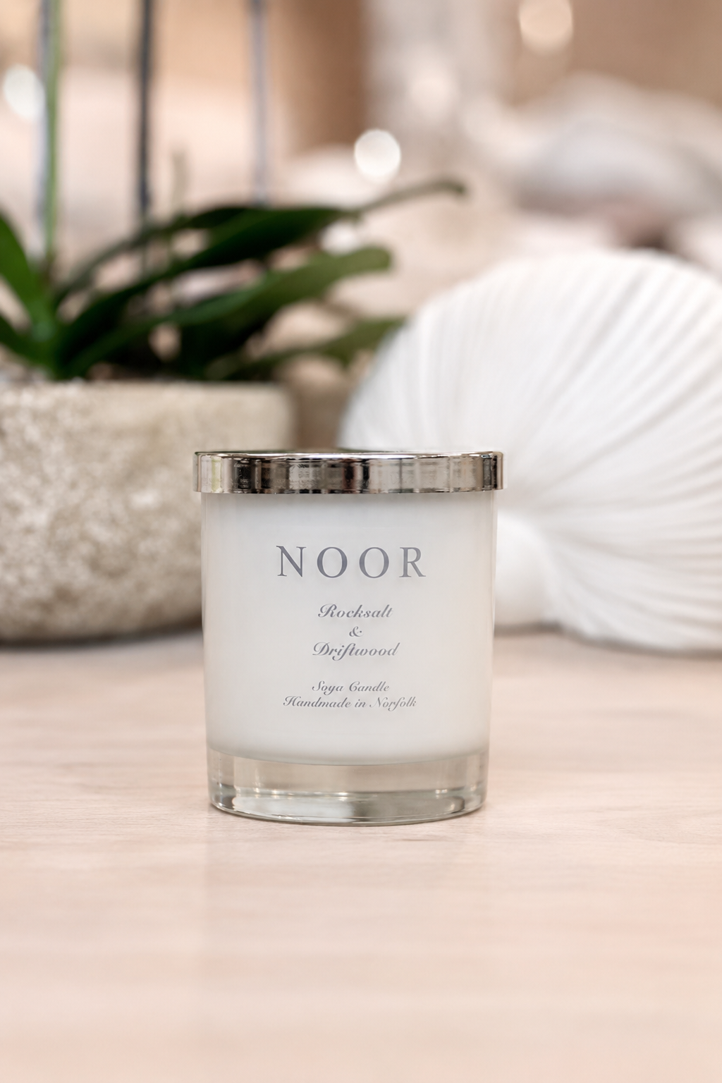 A white soy candle in a clear glass jar with a silver metallic lid, labeled &