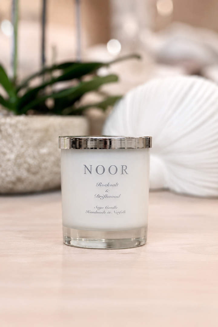 A white soy candle in a clear glass jar with a silver metallic lid, labeled &