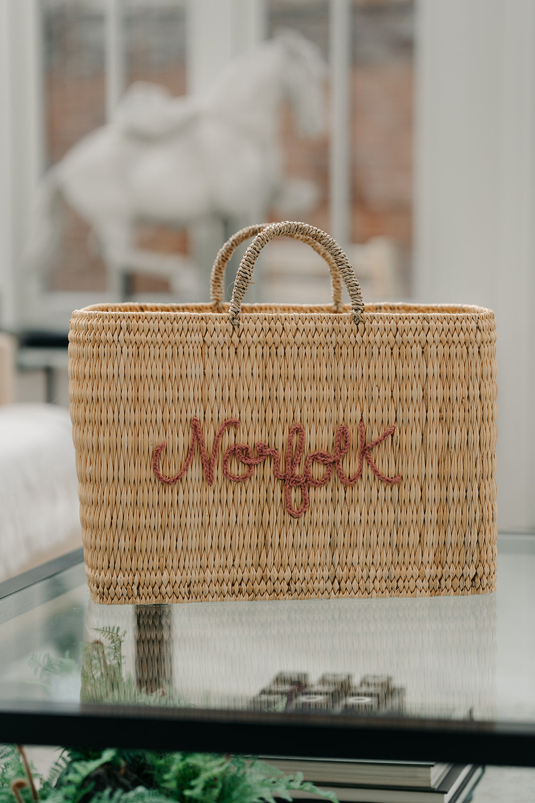 A natural woven straw tote bag with two top handles and the word &