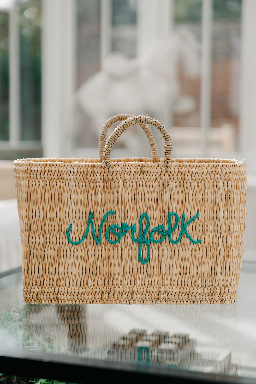 A natural woven straw tote bag with two rolled handles and the word &