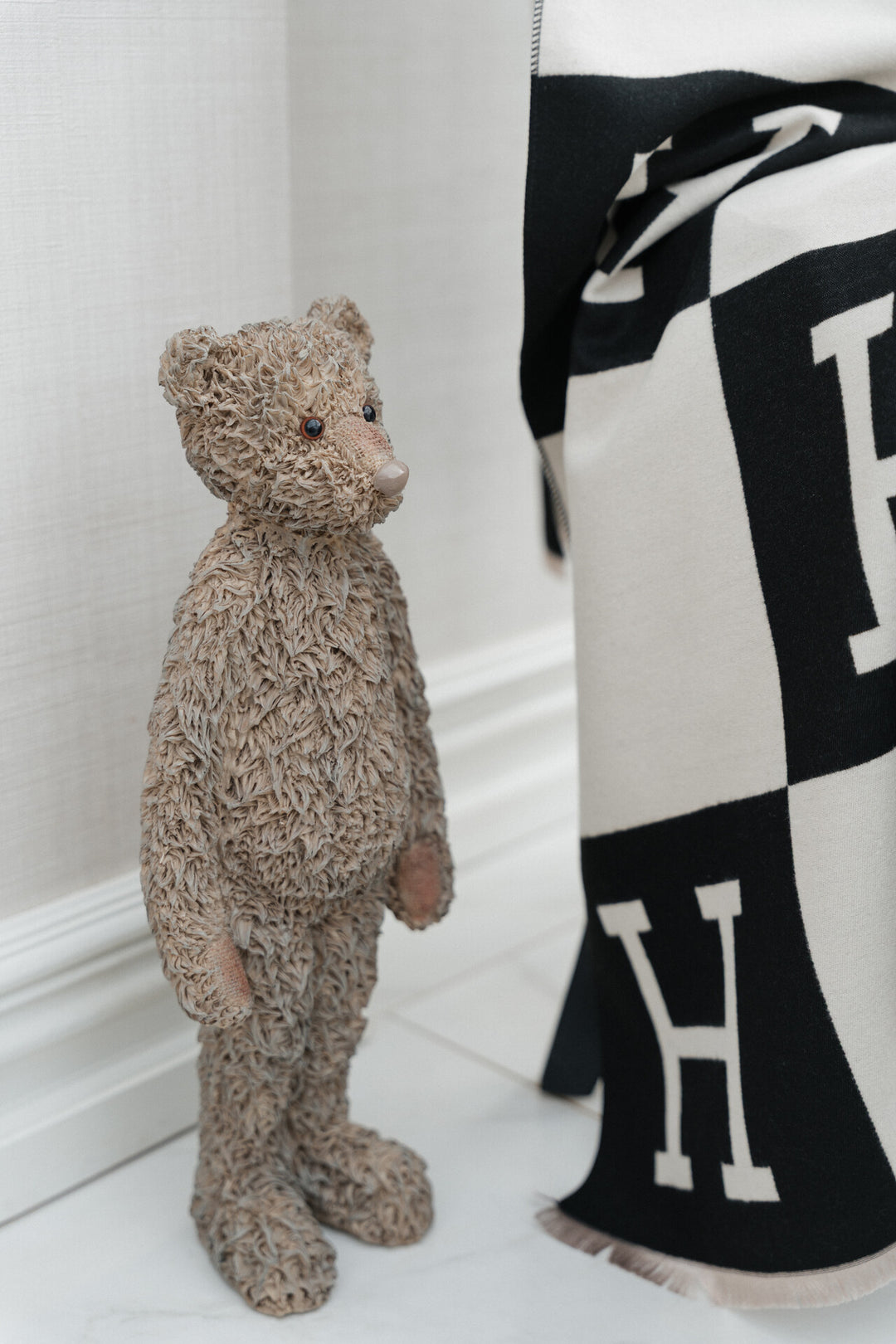 Teddy bear standing next to a black and white patterned fabric with &