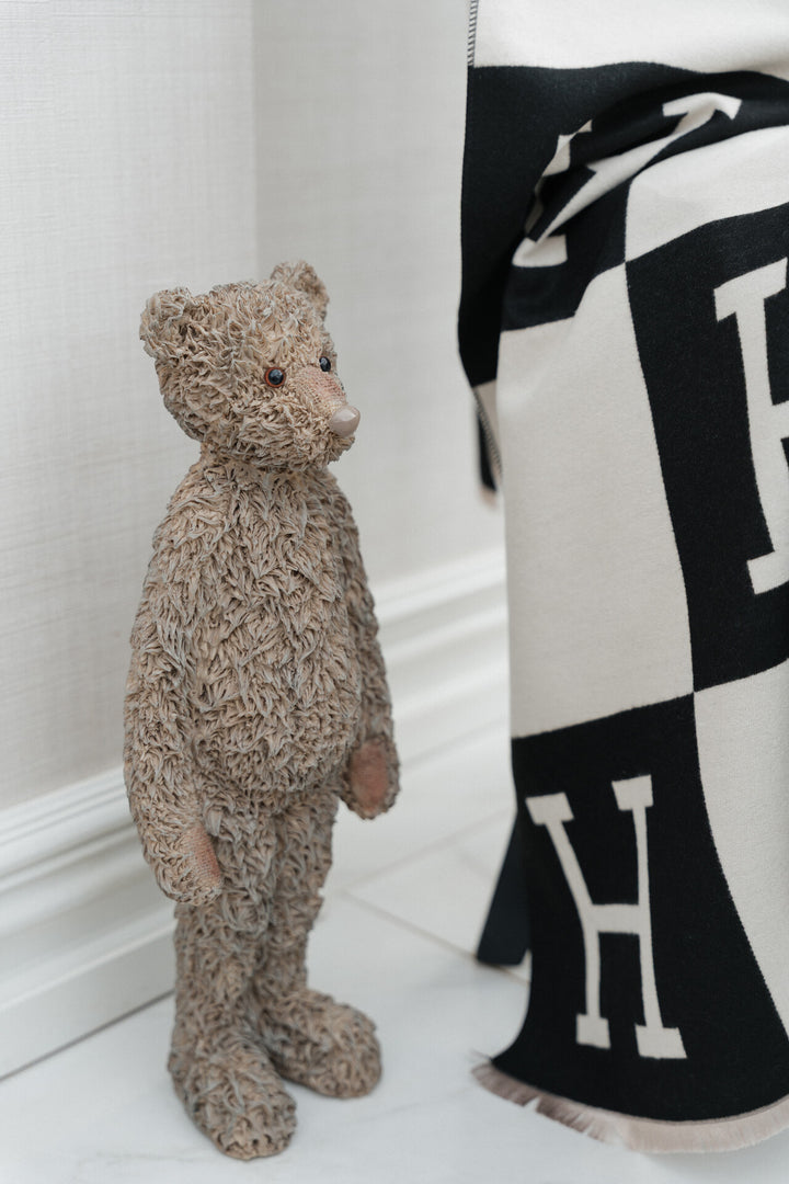 Teddy bear standing next to a black and white patterned fabric with &