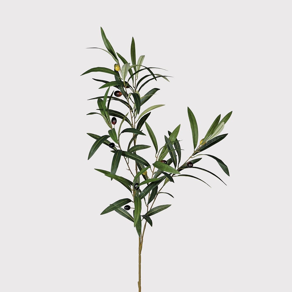 A single artificial olive branch with green and silver leaves and small dark olives, photographed against a plain light gray background.