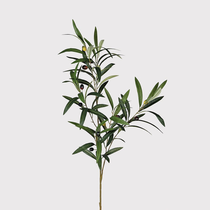 A single artificial olive branch with green and silver leaves and small dark olives, photographed against a plain light gray background.