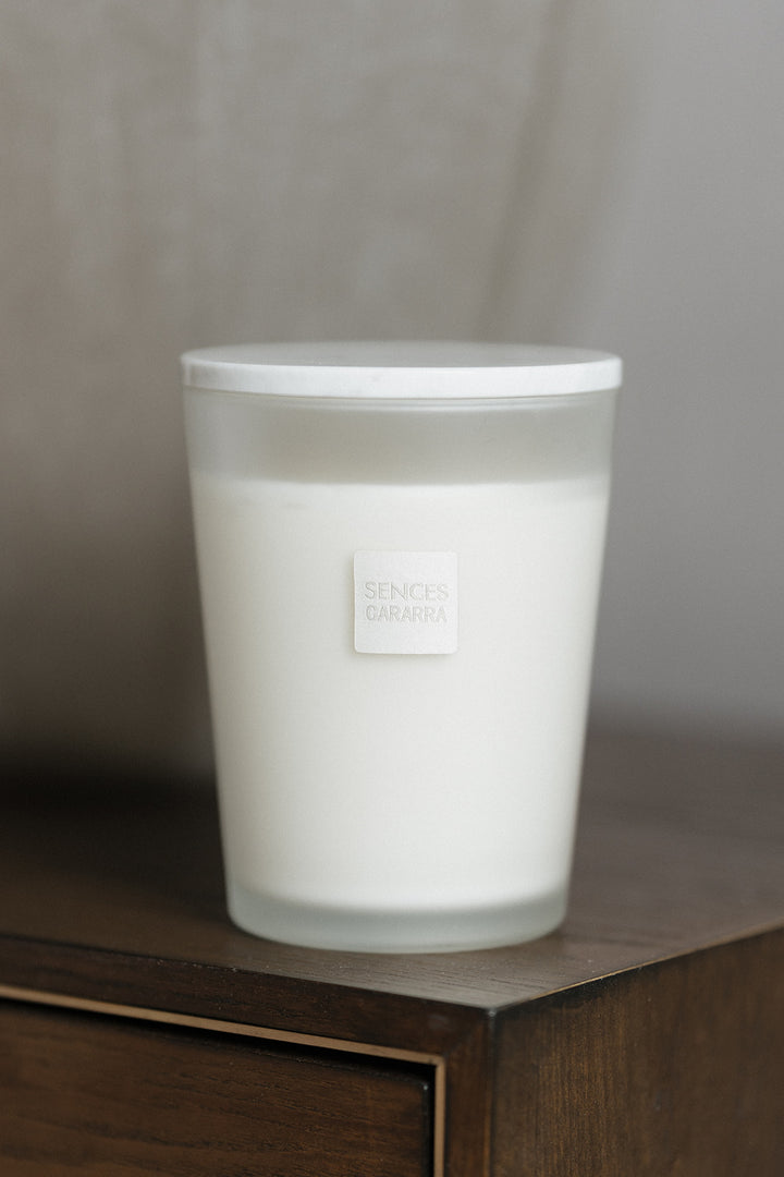 A frosted glass jar candle with a white lid and a small square label reading &