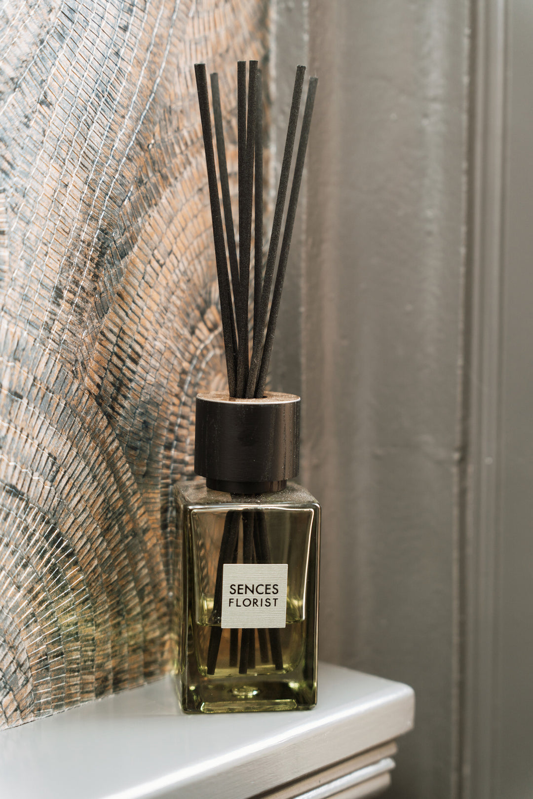 Reed diffuser with 'Sences Florist' label on a surface with a textured wall background