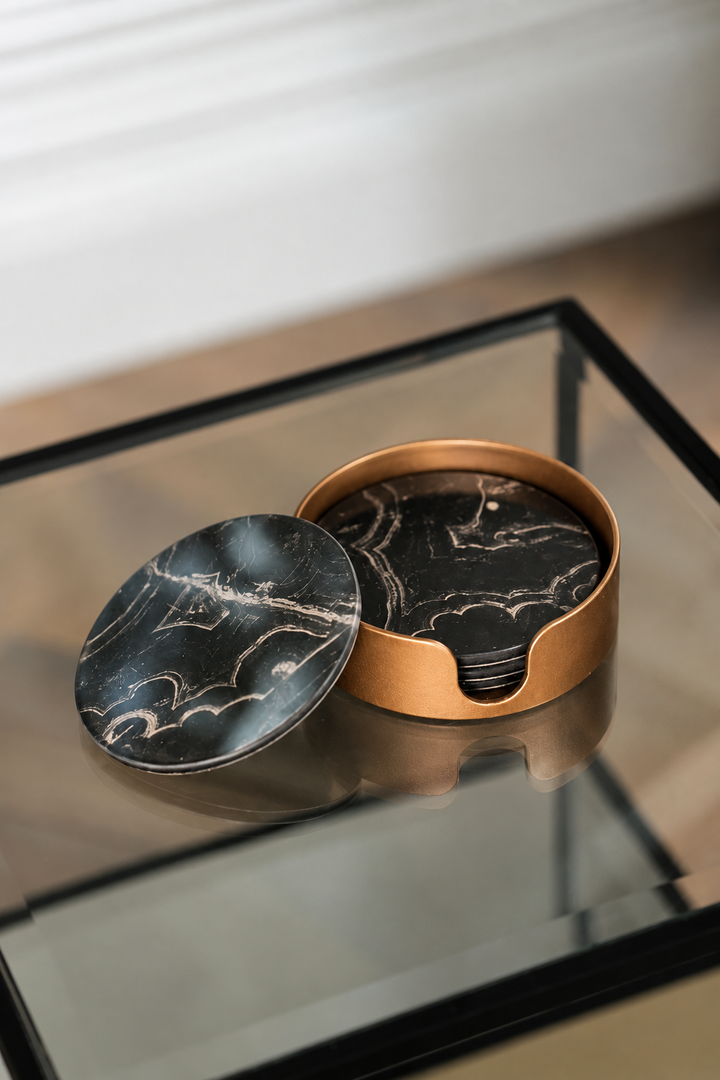 A round black marble-patterned tray with a matching circular base and a copper-toned outer rim, shown on a glass tabletop in an indoor setting.